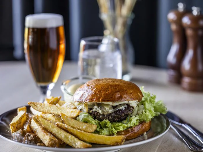 En tallerken med en cheeseburger, salat og pommes frites står på et bord ved siden af et glas øl, et glas vand og salt- og peberbøsser i baggrunden.