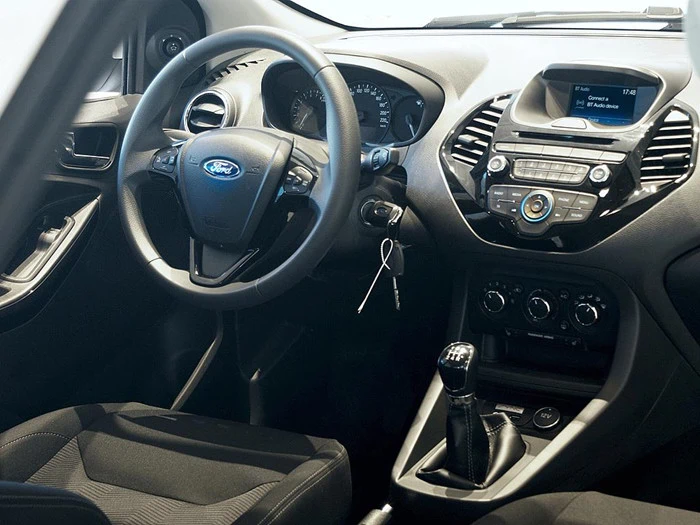 Interiørbillede af en Ford-bil med rat, instrumentbræt med touchscreen-display, manuelt gearskifte, betjeningsknapper og nøgler, der hænger fra tændingen.