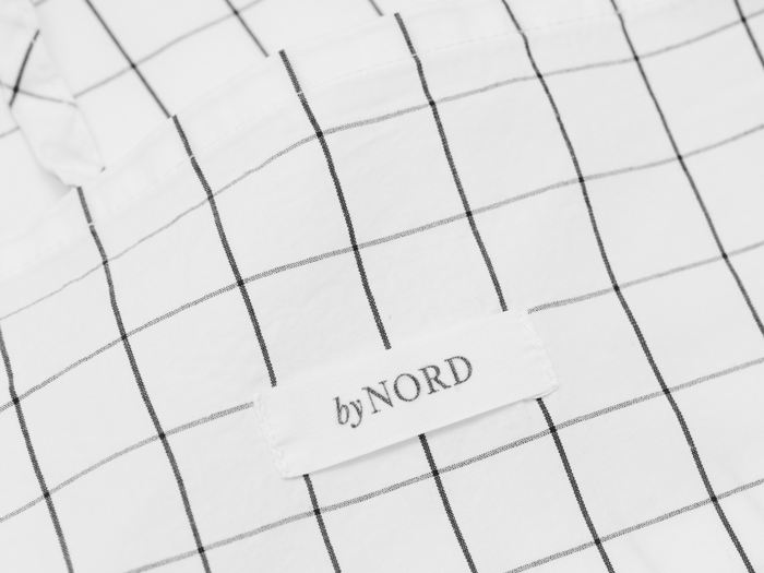 Et hvidt stof med et sort gittermønster og en påsyet etiket med teksten byNORD.