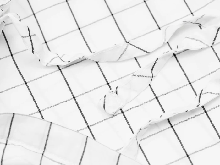 Et nærbillede af hvidt stof med et sort gittermønster, der viser en knap og en del af en krave, sandsynligvis fra en skjorte.