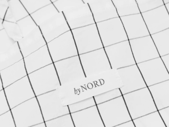 Et hvidt stof med et sort gittermønster og en påsyet etiket med teksten byNORD.