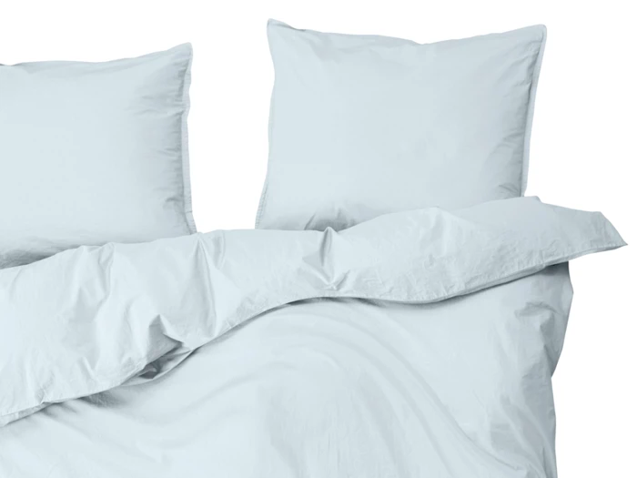 To hvide puder og en hvid dyne på en pænt redt seng, set ovenfra mod en almindelig hvid baggrund.