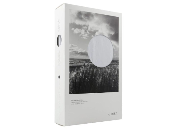 Hvid rektangulær produktæske med et sort-hvidt landskabsfoto, en cirkulær udskæring, der viser hvidt stof indeni, og mærket by NORD trykt i bunden.