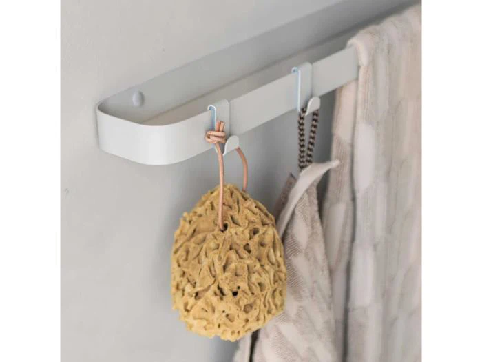 En beige svamp, et stribet håndklæde og et lyst ternet håndklæde hænger på kroge på en moderne hvid væghængt skinne.