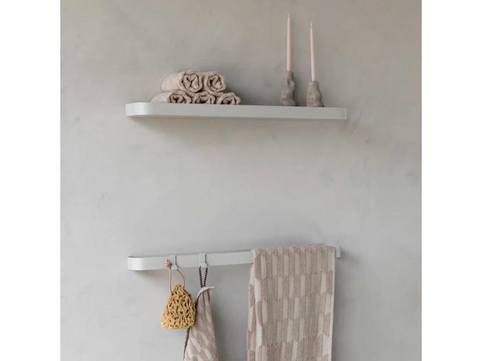 Minimalistisk badeværelsesindretning med en hvid hylde med rullede håndklæder og to stearinlys, og en håndklædeholder nedenunder med et beige håndklæde og hængende badetilbehør.
