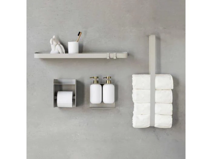 Minimalistisk vægopsætning på badeværelset med en hylde med tandbørsteholder og dekoration, en toiletpapirrulleholder, sæbedispensere og en strop med stablede toiletpapirruller.