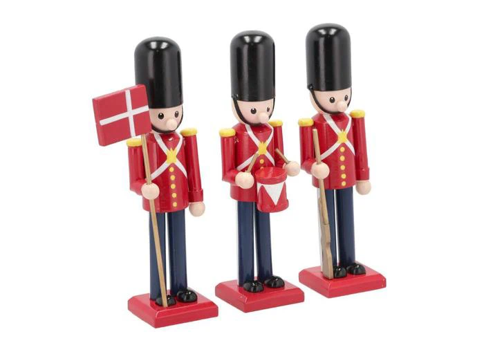 Tre legetøjssoldatfigurer i røde uniformer og høje sorte hatte; den ene holder et dansk flag, den anden en tromme og den sidste et gevær.