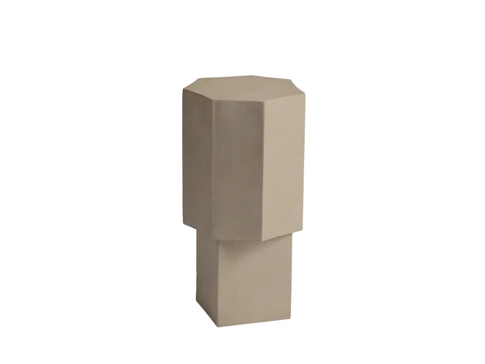 En beige, geometrisk skulptur med en ottekantet top og en rektangulær base, der står oprejst på en ensfarvet hvid baggrund.