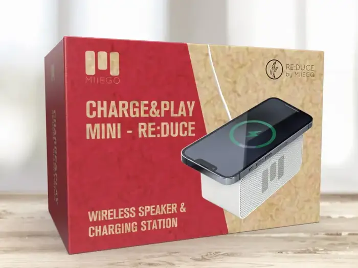 Rød og beige æske med MIIEGO Charge&Play Mini RE:DUCE, en trådløs højttaler og ladestation, med et billede af en telefon, der oplader oven på højttaleren.