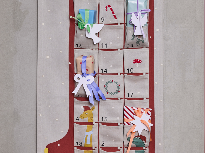 En adventskalender i stof formet som en strømpe med nummererede lommer, hvoraf nogle indeholder indpakkede gaver, en sukkerstang, en udklippet due og dyreillustrationer.