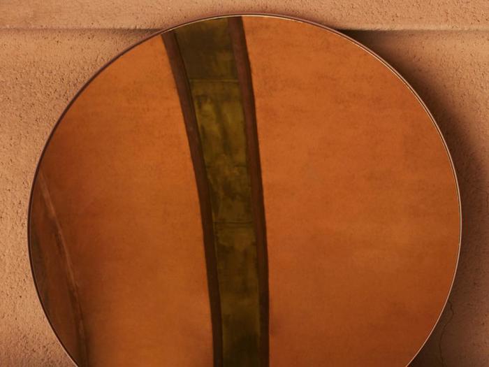 Et rundt spejl reflekterer en orangebrun væg og en lodret grønlig stribe, hvilket skaber en abstrakt komposition.