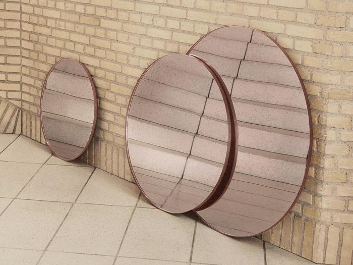 Tre runde spejle i forskellige størrelser læner sig op ad en hjørnevæg af beige mursten og reflekterer klinkegulvet og en del af væggen.