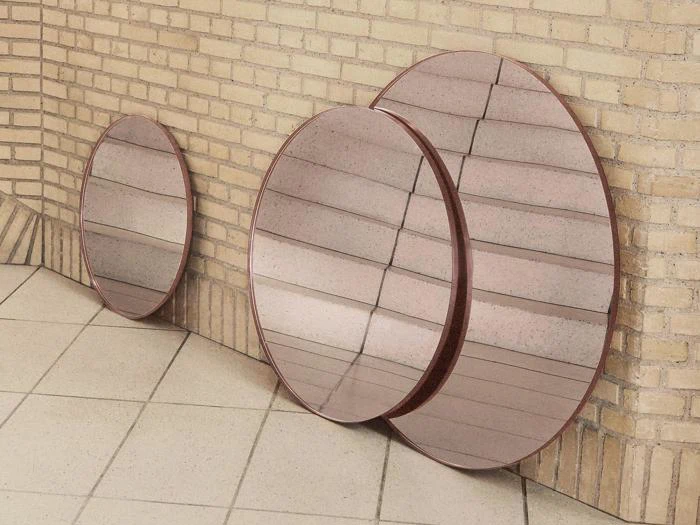 Tre runde spejle i forskellige størrelser læner sig op ad en hjørnevæg af beige mursten og reflekterer klinkegulvet og en del af væggen.