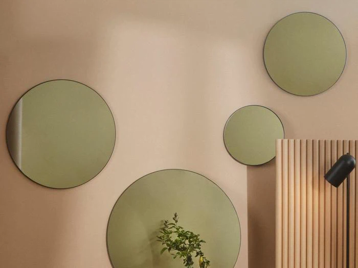 Fire runde spejle i forskellige størrelser er monteret på en beige væg; en plante og en sort lampe er delvist synlige i nederste højre hjørne.