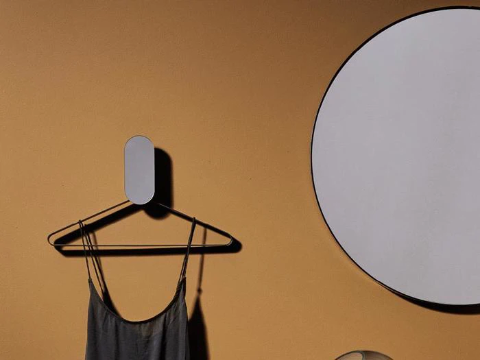 En minimalistisk scene med en grå kjole på en bøjle, et rundt spejl og en solbrun væg i baggrunden.