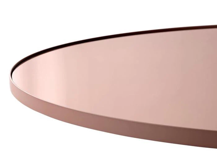 Nærbillede af en rund, pink metalbordplade med hævet kant, vist i en vinkel mod en hvid baggrund.