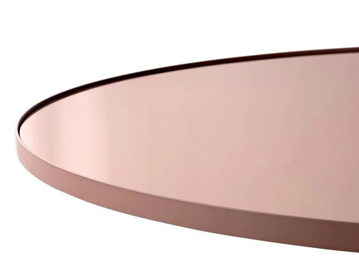 Nærbillede af en rund, rosaguld- eller kobberfarvet metalbakke eller bordplade med en glat, reflekterende overflade mod en hvid baggrund.