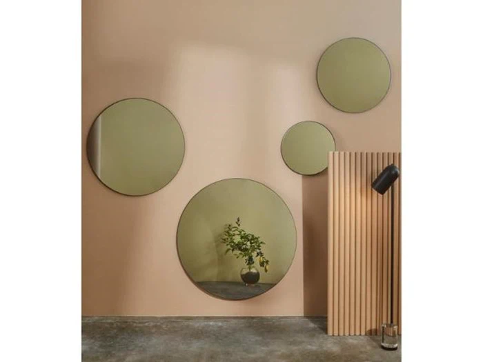 Fire runde spejle i forskellige størrelser er monteret på en beige væg og reflekterer en vase med planter. Et træpanel og en sort væglampe er på højre side.