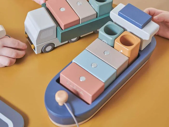 Børnehænder, der leger med farverige træklodser formet som en lastbil og en båd på en gul overflade.