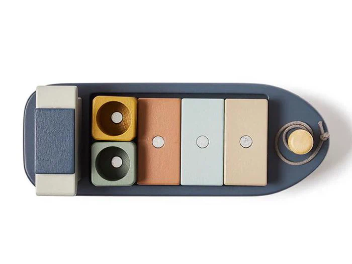 En legetøjsbåd af træ med stabelbare, farverige geometriske klodser og en træksnor, set ovenfra på en hvid baggrund.