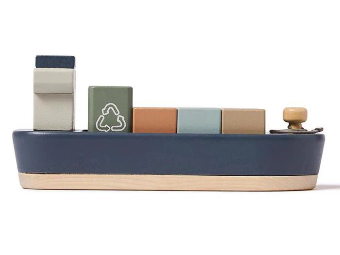 Legetøjsbåd af træ med farverige rektangulære klodser på toppen, bl.a. en med et hvidt genbrugssymbol. Båden er blå med en base af naturtræ og en lille træknap foran.