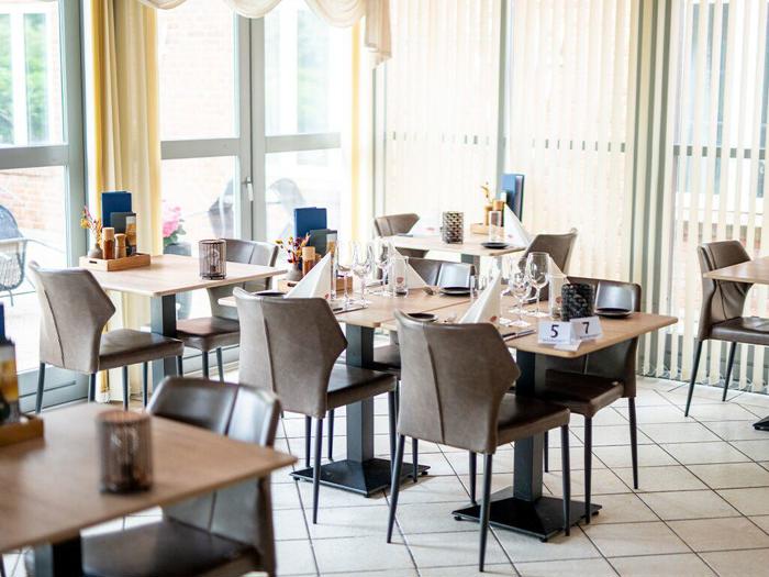 Moderne restaurant med borde dækket med glas, servietter og bestik. Naturligt lys strømmer ind gennem store vinduer og skaber en lys og indbydende atmosfære.