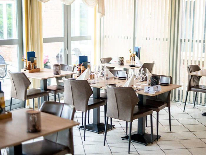 Moderne restaurant med borde dækket med glas, servietter og bestik. Naturligt lys strømmer ind gennem store vinduer og skaber en lys og indbydende atmosfære.