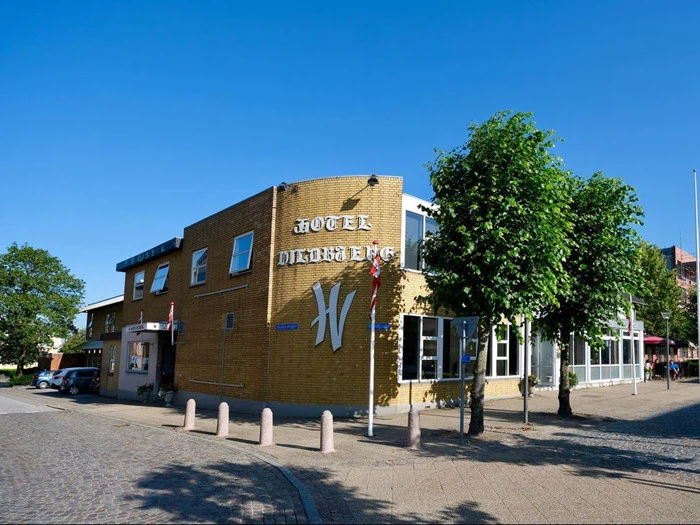 En toetagers gul murstensbygning med Hotel Duxiana-skilt, træer og en klar blå himmel i baggrunden.