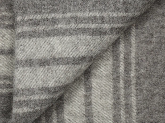 Nærbillede af et foldet, blødt, grå- og hvidstribet uldtæppe, der viser dets struktur og rektangulære mønster.
