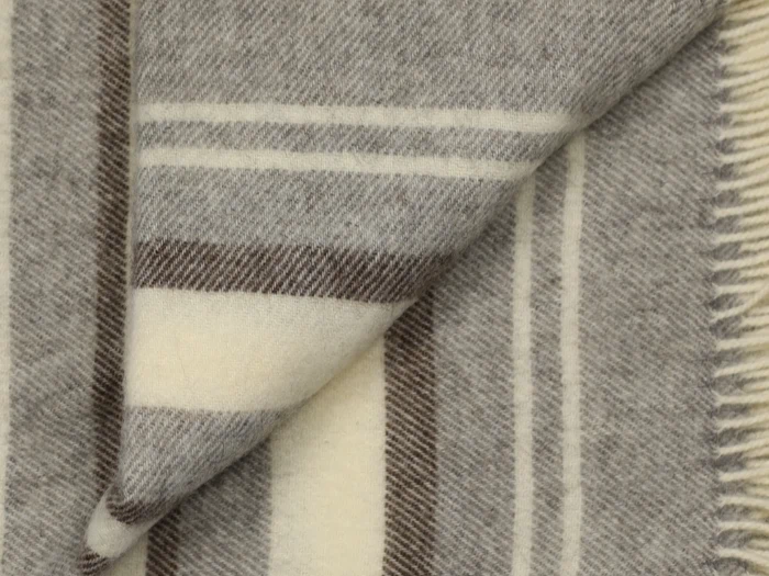 Nærbillede af et uldtæppe med beige, brune og cremefarvede striber og et foldet hjørne, der viser den bløde tekstur og frynsekanten.