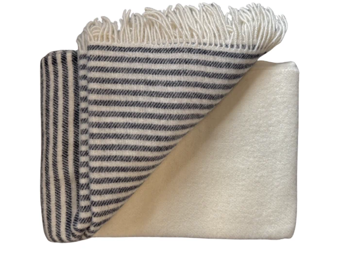 Et foldet uldtæppe med sort-hvide striber på den ene side og ensfarvet hvid på den anden, med frynsede kanter.