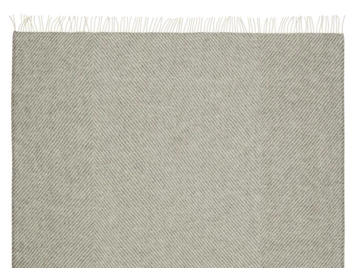 Et beige vævet tæppe med et diskret diagonalt sildebensmønster og frynsede kanter langs toppen.