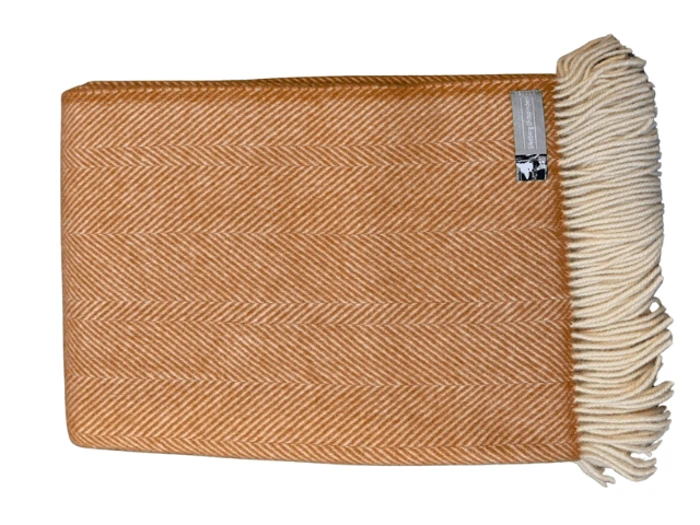 Et foldet, brunfarvet sildebensuldtæppe med cremefarvede frynser i den ene ende og en påsat etiket.