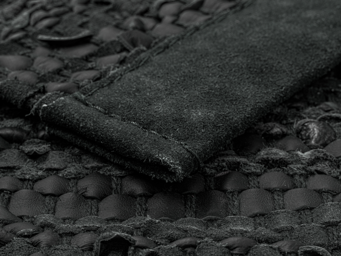 Nærbillede af et struktureret sort læder- og ruskindsmateriale med synlige syninger og vævede mønsterdetaljer.