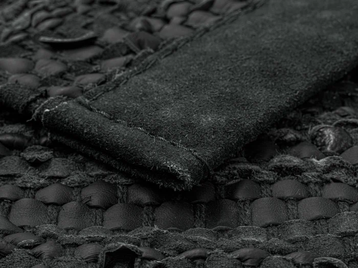 Nærbillede af et struktureret sort læder- og ruskindsmateriale med synlige syninger og vævede mønsterdetaljer.