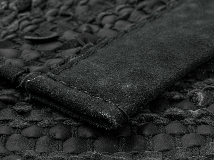 Nærbillede af et tekstureret sort læder- og ruskindsmateriale, der viser detaljerede syninger og et vævet mønster.