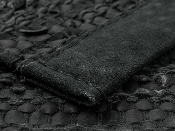 Nærbillede af et tekstureret sort læder- og ruskindsmateriale, der viser detaljerede syninger og et vævet mønster.