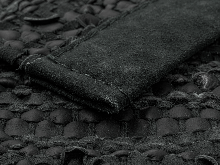 Nærbillede af et struktureret sort vævet stof med en hævet ruskindsstribe syet på tværs af overfladen.