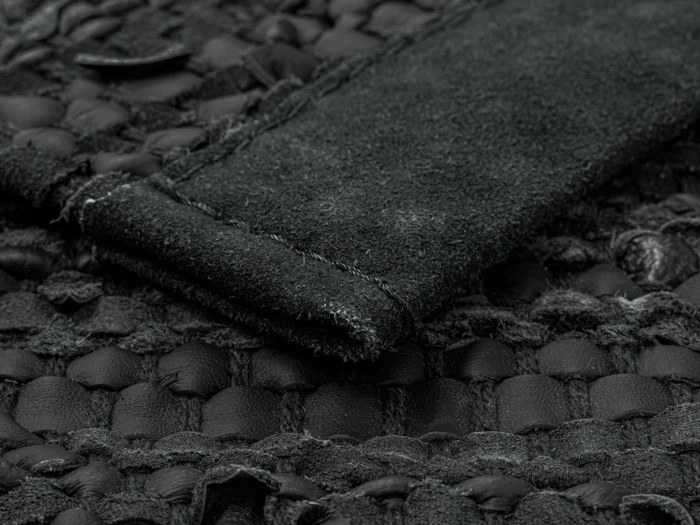 Nærbillede af et struktureret sort vævet stof med en hævet ruskindsstribe syet på tværs af overfladen.