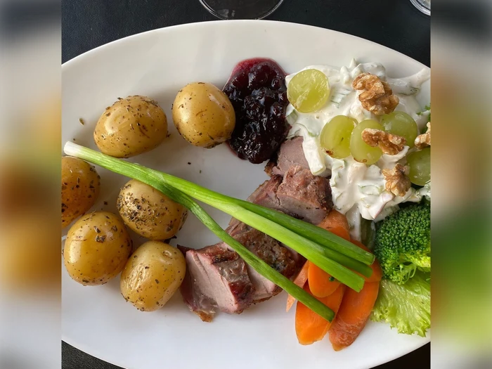 En oval tallerken med ristede kartofler, stegt kød i skiver, forårsløg, gulerødder, broccoli, salat, drue- og valnøddesalat og en klat bærsauce.