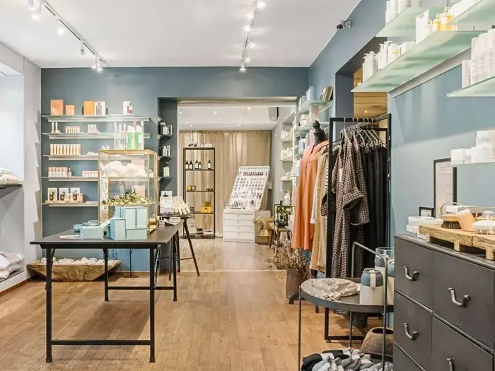 En stilfuld butiksindretning med trægulve, hylder med hudplejeprodukter, tøjstativer og et centralt udstillingsbord. Rummet er godt oplyst og pænt organiseret.