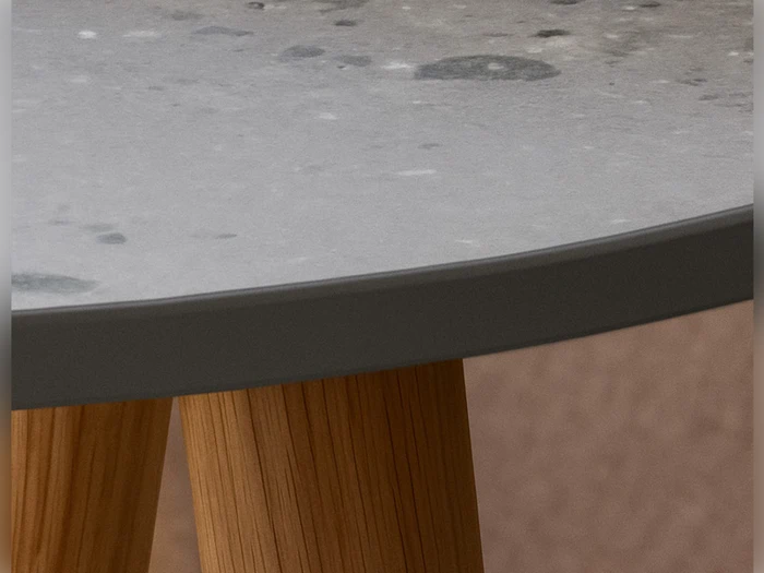 Nærbillede af et rundt bord med en grå, spættet stenplade og træben, vist mod en neutral baggrund.