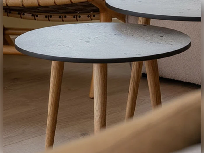 To runde sideborde med lyse stenplader og træben på et trægulv med en del af en kurvestol og en lys sofa i baggrunden.