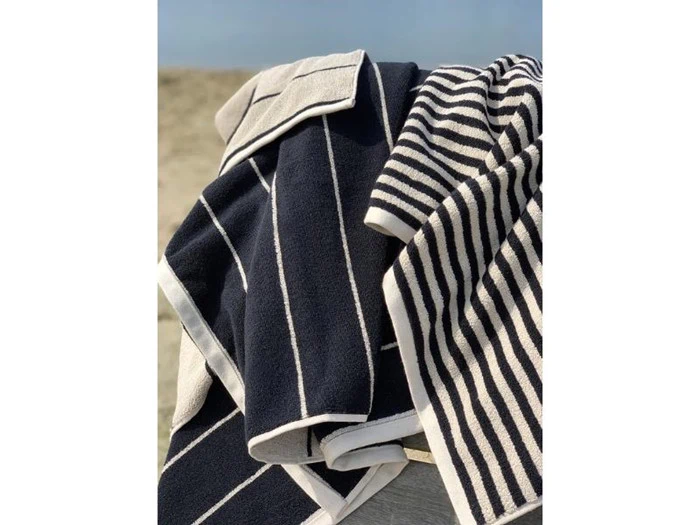 Tre sort- og hvidstribede håndklæder er draperet over en overflade udendørs med sandbaggrund og klar himmel.