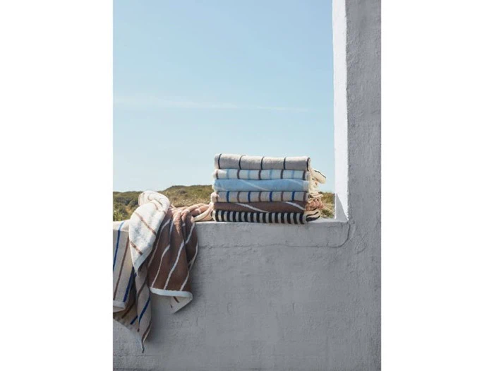 En stak foldede, stribede håndklæder ligger på en hvid afsats med blå himmel og grønne planter i baggrunden.