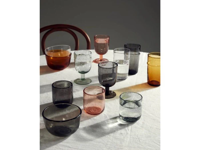 En samling af glas i forskellige farver – herunder glas, skåle og vinglas – anbragt på en hvid dug.
