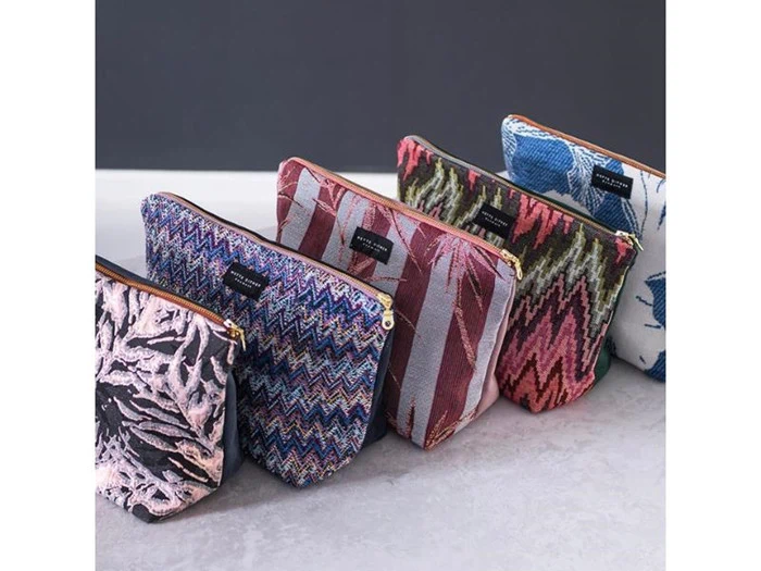 Fem mønstrede lynlåsposer står på rad og række, hver med et unikt, farverigt design på stof mod en ensfarvet baggrund.