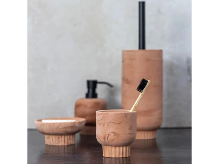 Et badeværelsessæt i træ med en tandbørste i en kop, en sæbedispenser, en sæbeskål og en toiletbørsteholder på en mørk overflade.