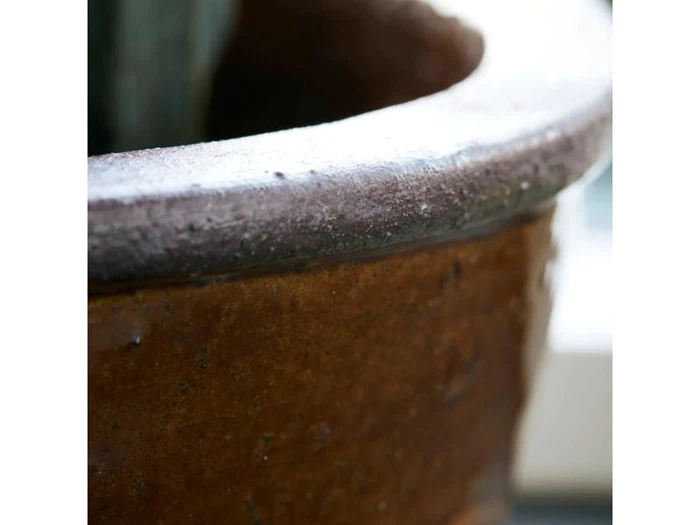 Nærbillede af den strukturerede kant og oversiden af en brun keramikpotte med blødt naturligt lys og sløret baggrund.