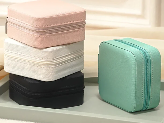 Fire små firkantede kufferter med lynlås i pastelrosa, hvid, sort og mintgrøn er arrangeret på en bakke, hvor den ene står oprejst.